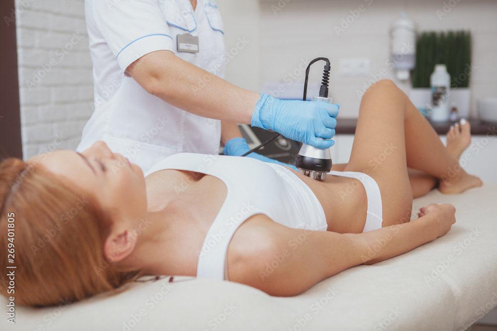 Obraz premium Attractive woman with slim body getting rf-lifting treatment on her belly. Female client receiving anti-cellulite skin firming procedure by cosmetologist. Skincare, fat reduction concept