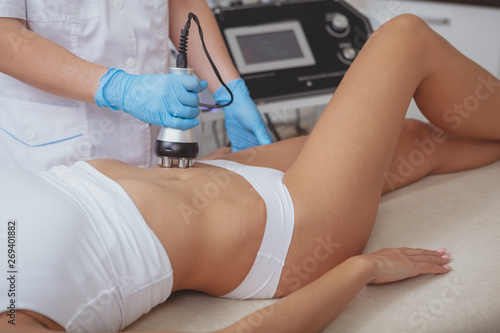 Cropped shot of a professional dermatologist performing radiofrequency lifting procedure on the stomach of a woman. Female client getting rf-lifting treatment on her belly at cosmetology clinic photo