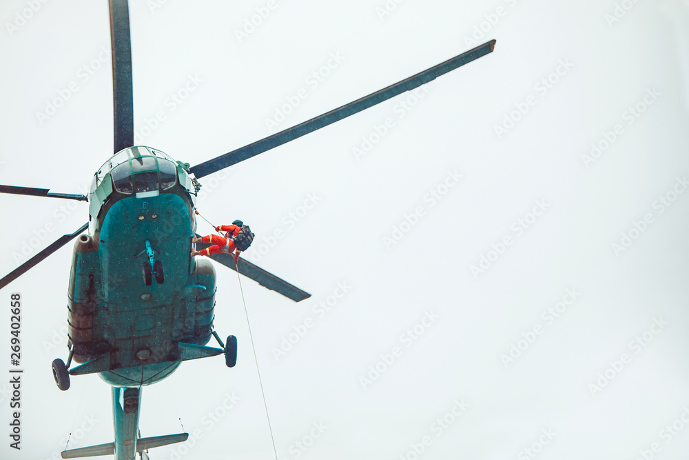 Rescue helicopter and rescuer on the rope - life-saving flying vehicle on the rainy sky background. Rescue helicopter and rescuer on the rope - life-saving flying vehicle on the rainy sky background.
