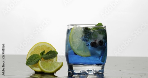 Glass with cold blue drink with leaves of mint, lime, lemon, black currants