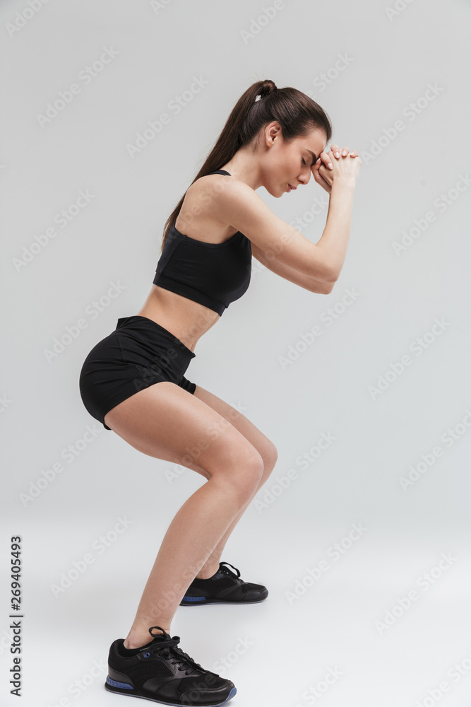 Naklejka premium Beautiful young sport fitness woman make exercises isolated over grey wall background.