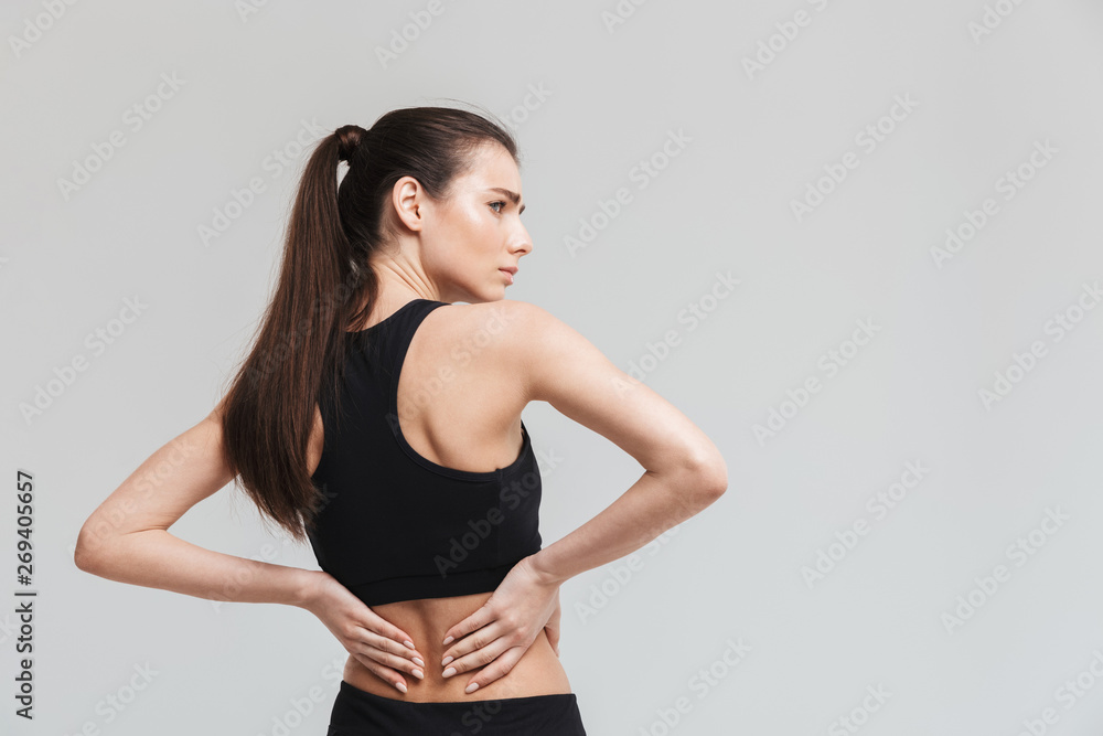 Beautiful young sad sport fitness woman with backache isolated over grey wall background. Beautiful young sad sport fitness woman with backache isolated over grey wall background.