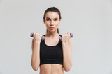 Young sport fitness woman make exercises with dumbbells isolated over grey wall background.