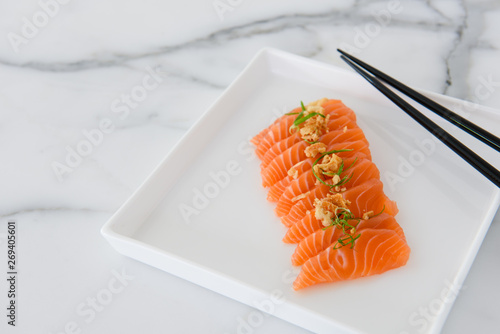 Sliced salmon sashimi on white plate with chopsticks and white background