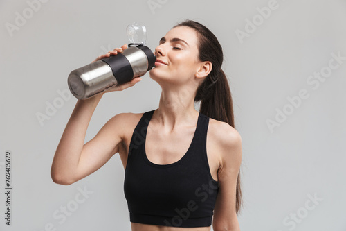 Beautiful young sport fitness woman drinking water isolated over grey wall background.