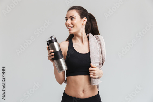 Fototapeta Naklejka Na Ścianę i Meble -  Beautiful young sport fitness woman drinking water isolated over grey wall background.