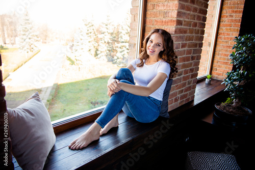 Portrait of her she nice-looking attractive lovely charming fit slim thin cheerful cheery wavy-haired girl sitting on window sill at industrial loft wooden brick style interior indoors