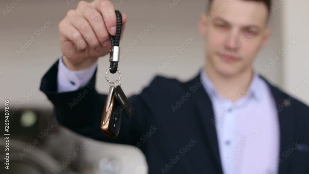 Close-up of a man in a suit holding the keys to a new car in a modern showroom. Auto business, car sale, technology and people concept. Close-up of a man in a suit holding the keys to a new car in a modern showroom. Auto business, car sale, technology and people concept.