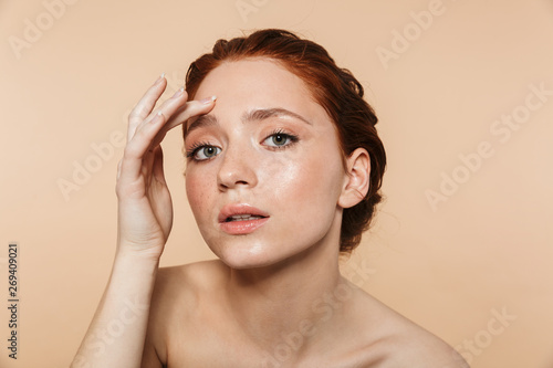 Pretty young redhead woman posing isolated over beige wall background looking at camera as a mirror.