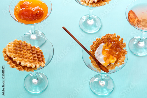 Creative idea, breakfast. Belgian waffles with jam and cream in martini glasses on pastel blue background, top view flat lay modern minimal composition