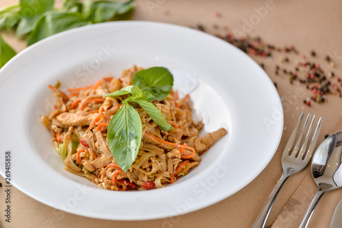 pasta with chicken and vegetables decorated with basil on a white plate