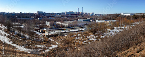 Panorama of an industrial area with a plant, smoking pipes of boilers and buildings of workshops in the winter valley with grass