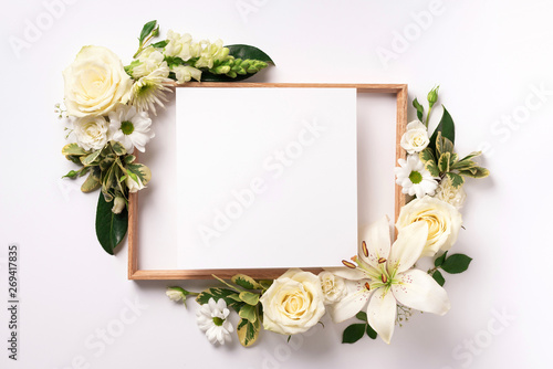 Creative layout with white flowers, square shape paper for copyspace over light background. Top view, flat lay. Spring and summer concept.