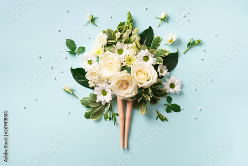 Doll legs and white rose, flowers, leaves on blue background. Contemporary art collage. Spa, body treatment and skin care concept. Top view. Creative layout photo