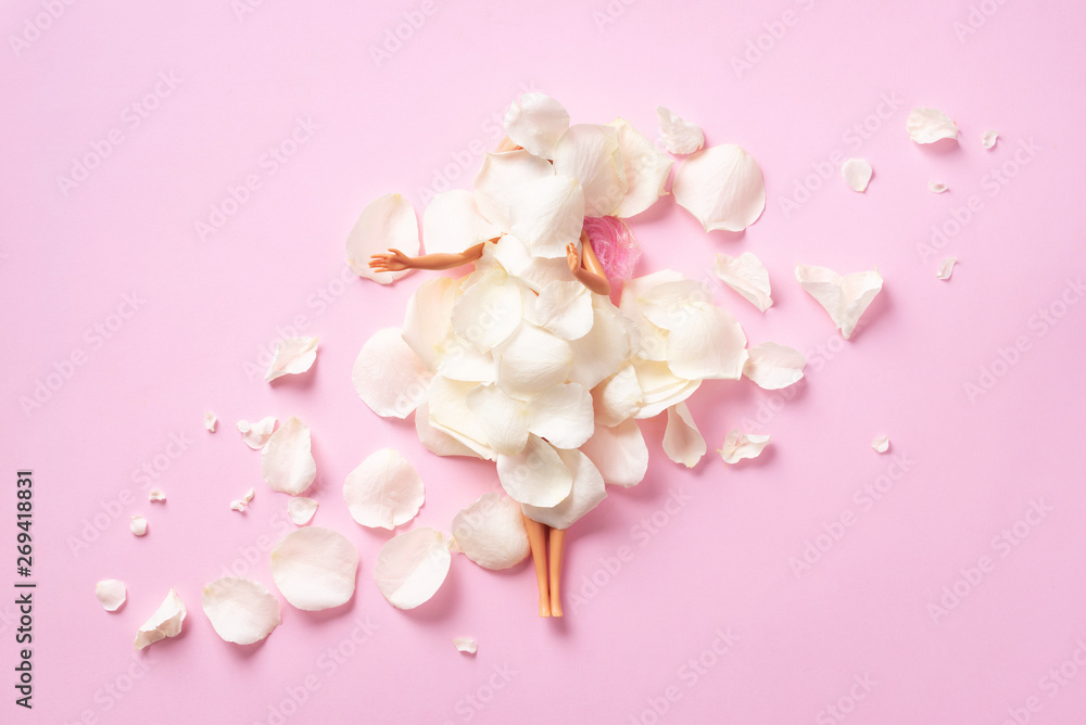 Obraz premium Girl doll under white rose petals. Gift for Women's day, Mother's day. Creative layout. Top view, flat lay. Minimal holiday concept