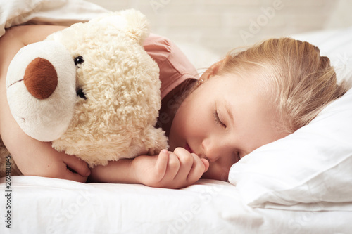 Cute little child girl sleeping with teddy bear in her bed