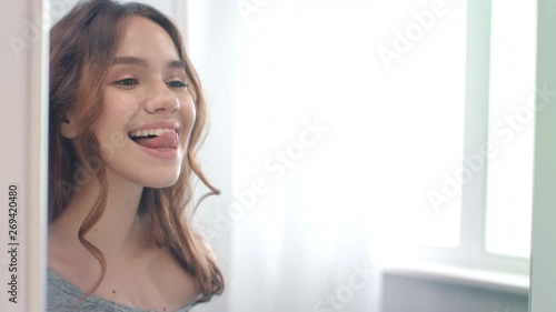 Smiling woman licking clean and white teeth front mirror in home bathroom