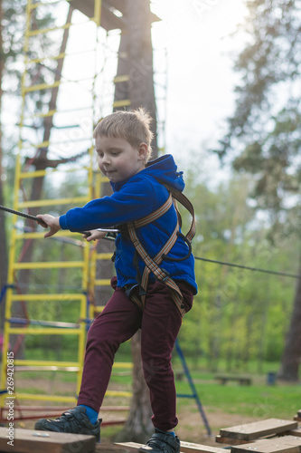 A little boy is training in a rope park. The child climbs the obstacle course. Active recreation in the park in the fresh air.
