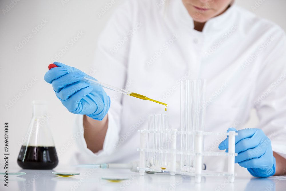 Scientist working with pharmaceutical cbd oil in a laboratory with glass dropper and a bowl Scientist working with pharmaceutical cbd oil in a laboratory with glass dropper and a bowl