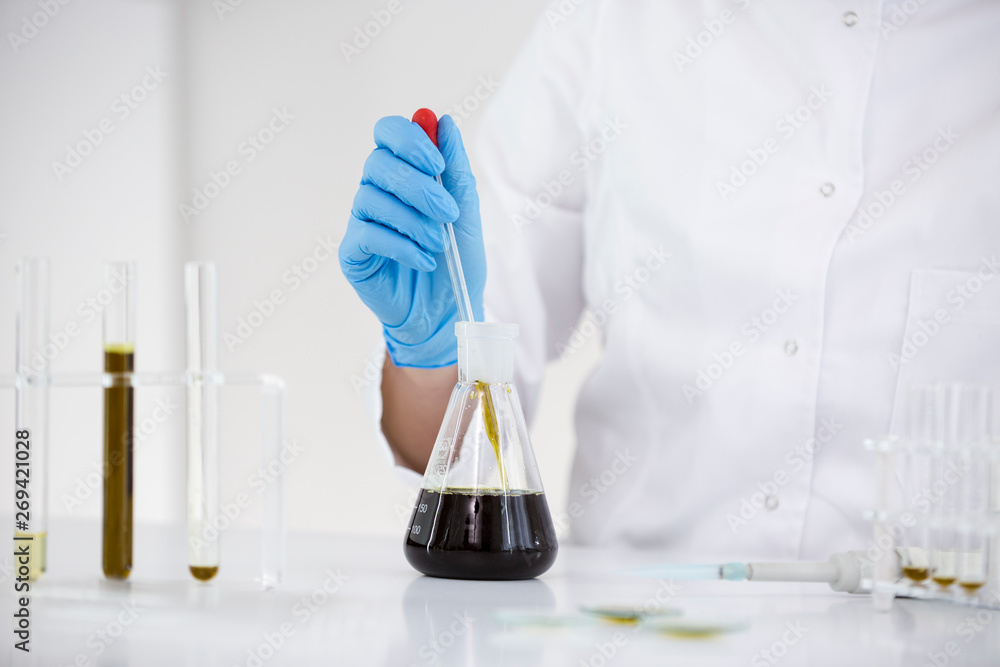 Scientist working with pharmaceutical cbd oil in a laboratory with glass dropper and a bowl Scientist working with pharmaceutical cbd oil in a laboratory with glass dropper and a bowl