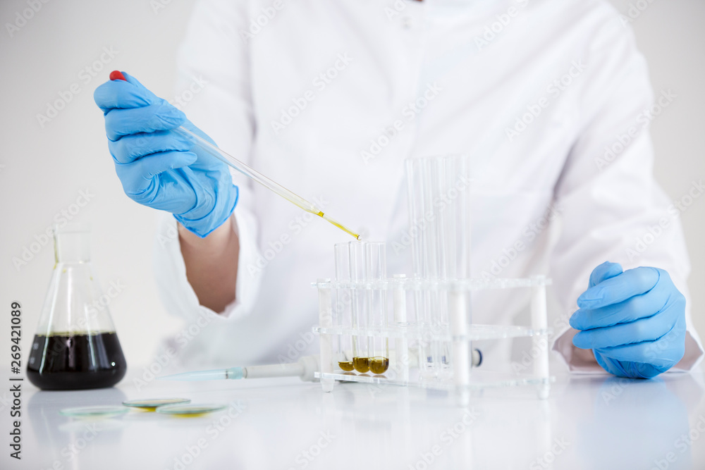 Scientist working with pharmaceutical cbd oil in a laboratory with glass dropper and a bowl Scientist working with pharmaceutical cbd oil in a laboratory with glass dropper and a bowl