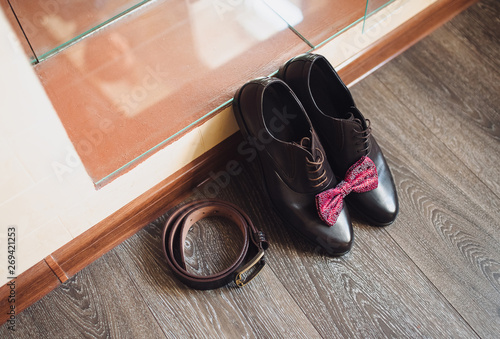 Wedding arrangement and concept. Shoes, red bowtie and leather belt lie on the background of the parquet. Morning groom.