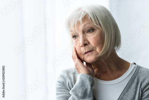 pensive senior woman with grey hair looking away at home