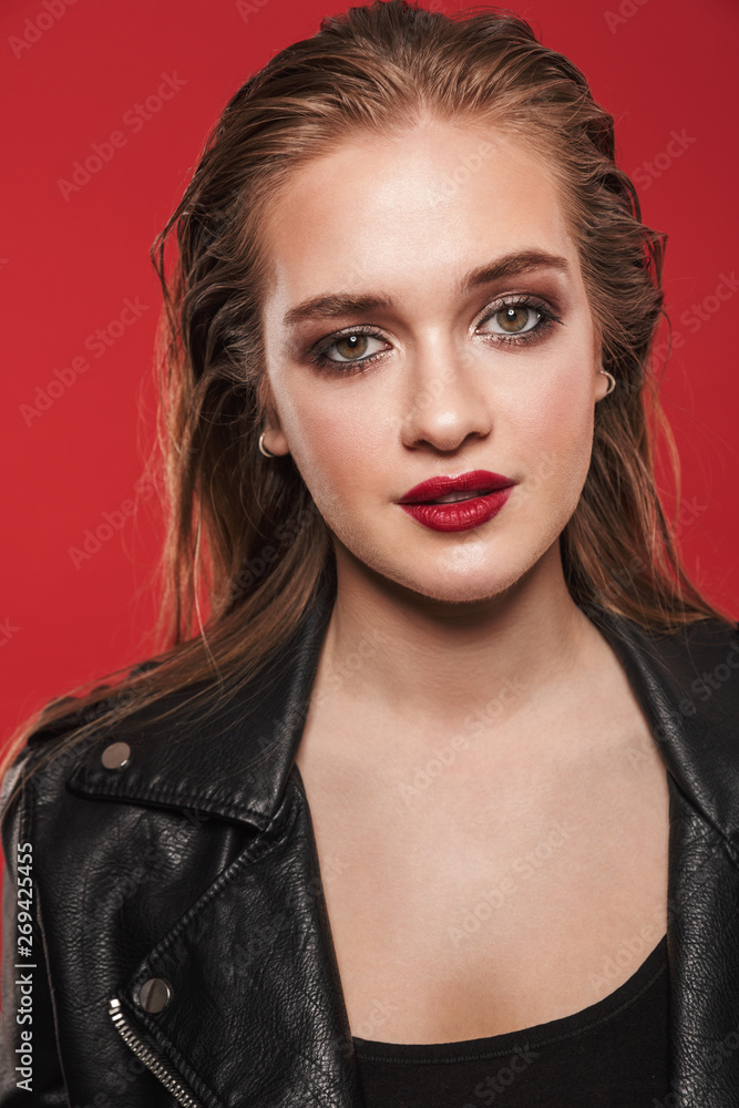 Fototapeta premium Beautiful young amazing woman with bright makeup red lipstick posing isolated over red wall background.