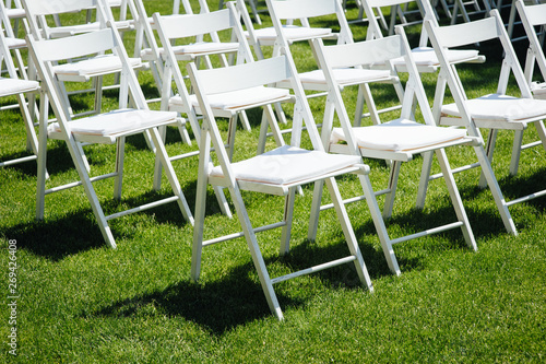 Rows of white folding chairs on lawn before a wedding ceremony in summer photo