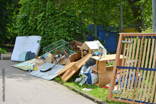 Bulky waste including old furniture, vacuum cleanerlying on grass next to street pavement