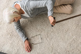 overhead view of sick senior woman with walking stick lying on carpet