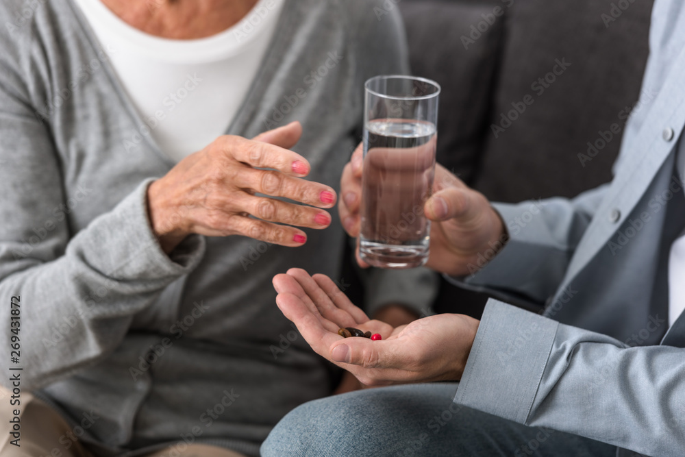 cropped view of man giving to senior mother glass of water and medicine cropped view of man giving to senior mother glass of water and medicine