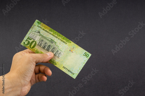 Hand holding saudi riyal bank notes on black background. Financial concept and selective focus