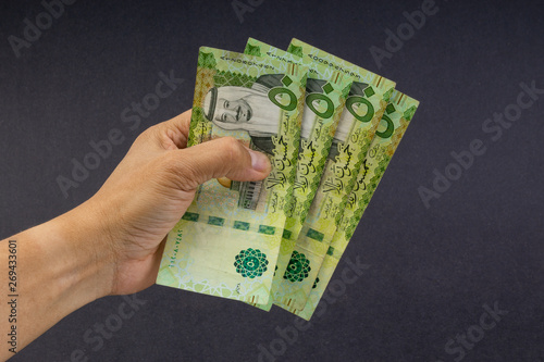 Hand holding saudi riyal bank notes on black background. Financial concept and selective focus