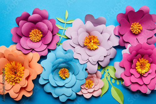 top view of colorful paper cut flowers with green leaves on blue background