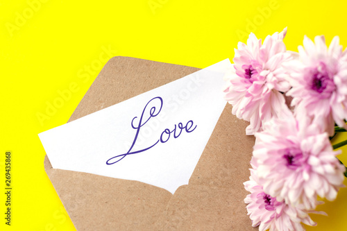 Love envelope and letter with written word love with pink chrysanthemum flowers on bright yellow bacground.