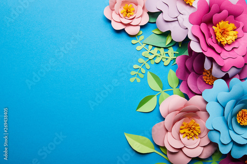 top view of colorful paper cut flowers with green leaves on blue background with copy space #269438405