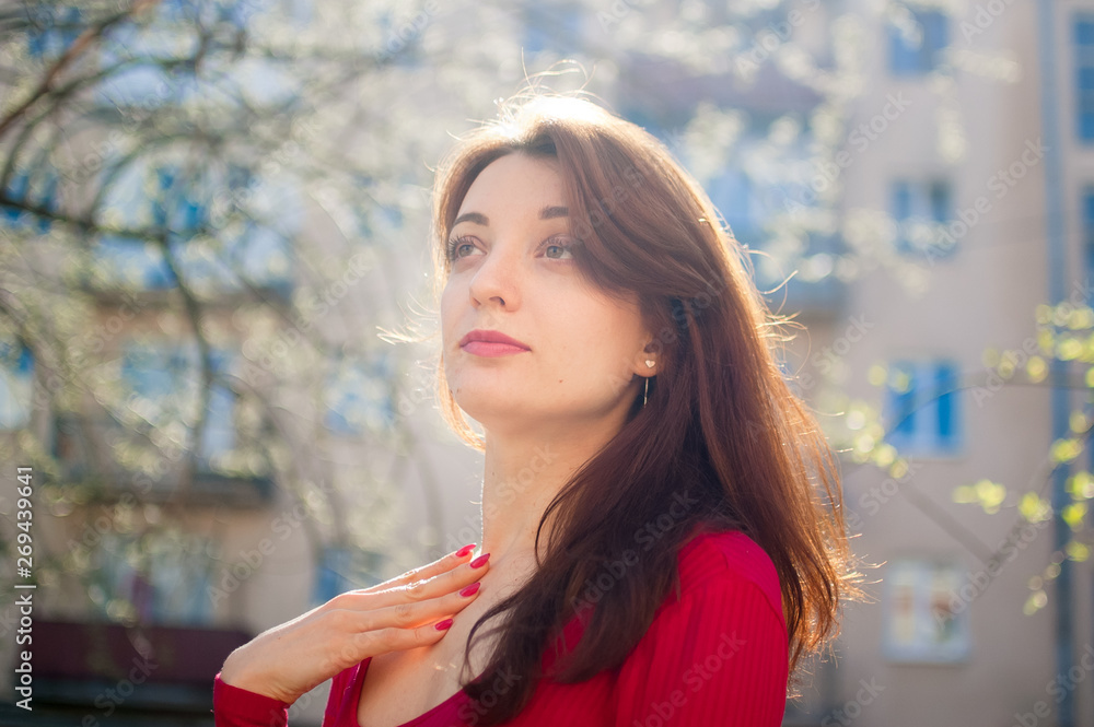 Obraz premium Beautiful close up portrait of young brunette woman with the wind blowing hair on buildings urban background.