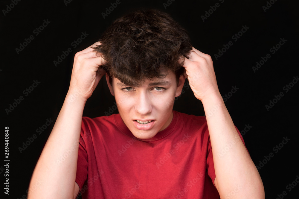Teenage boy with braces on his teeth on a dark background keeps his head and suffering because he has a headache Teenage boy with braces on his teeth on a dark background keeps his head and suffering because he has a headache