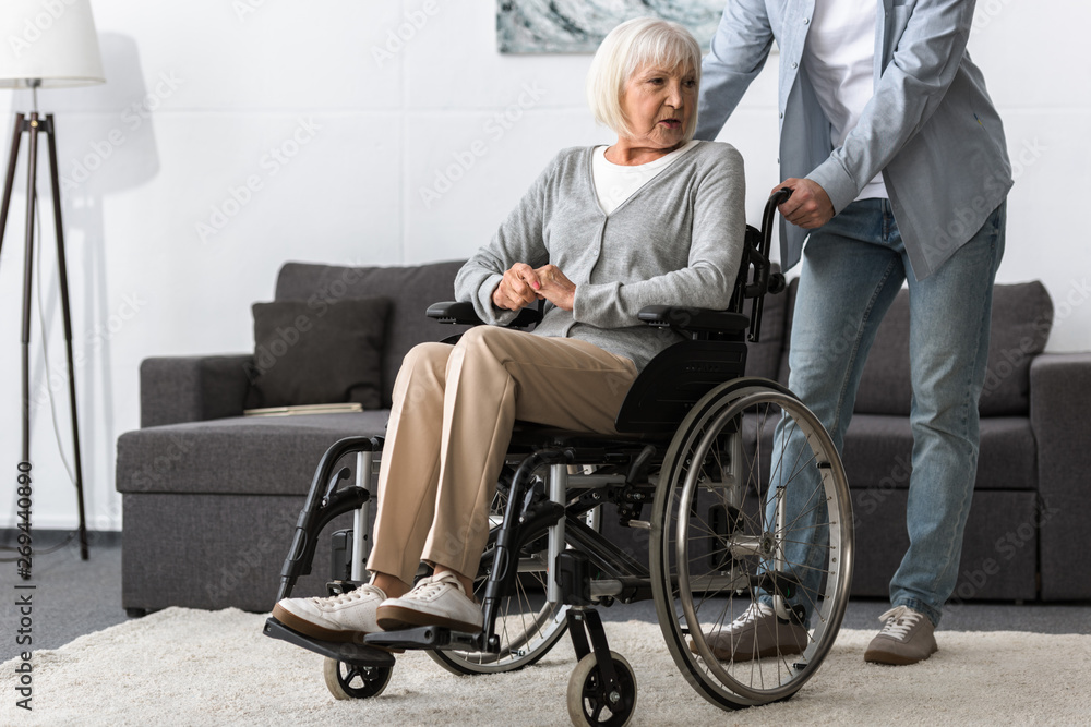 cropped view of man carrying senior mother on wheelchair cropped view of man carrying senior mother on wheelchair