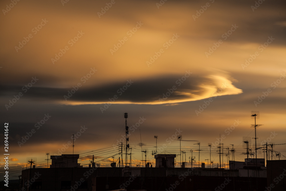 Dramatic clouds over rooftops filled with city aerials at sunset