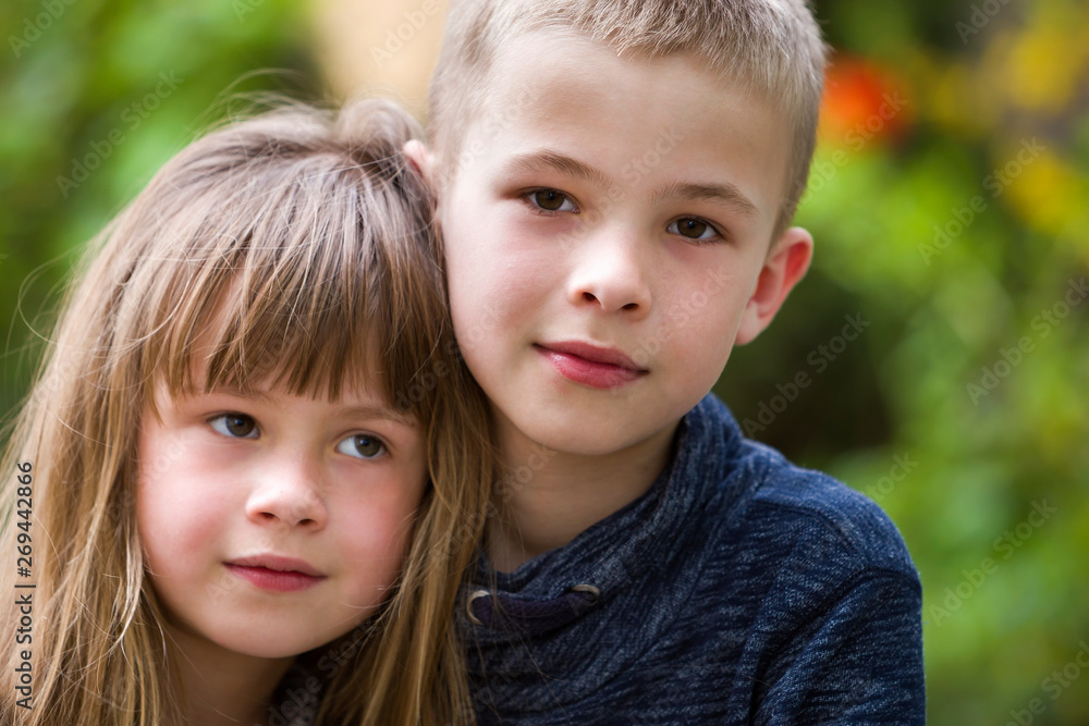 Two cute fair-haired children siblings, young boy brother and sister girl outdoors on bright sunny green bokeh background. Family relation, friendship and love concept.