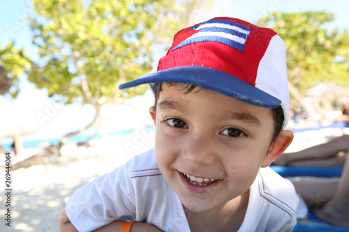 Portrait of a happy little boy with a smile on his face and a bright red cap on his head on the beach in the Caribbean. Summer, rest, vacation, holidays