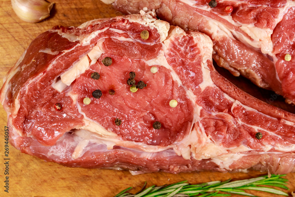 Raw fresh beef rib eye steak on bone with spices, garlic and rosemary on wooden table. Top view Raw fresh beef rib eye steak on bone with spices, garlic and rosemary on wooden table. Top view