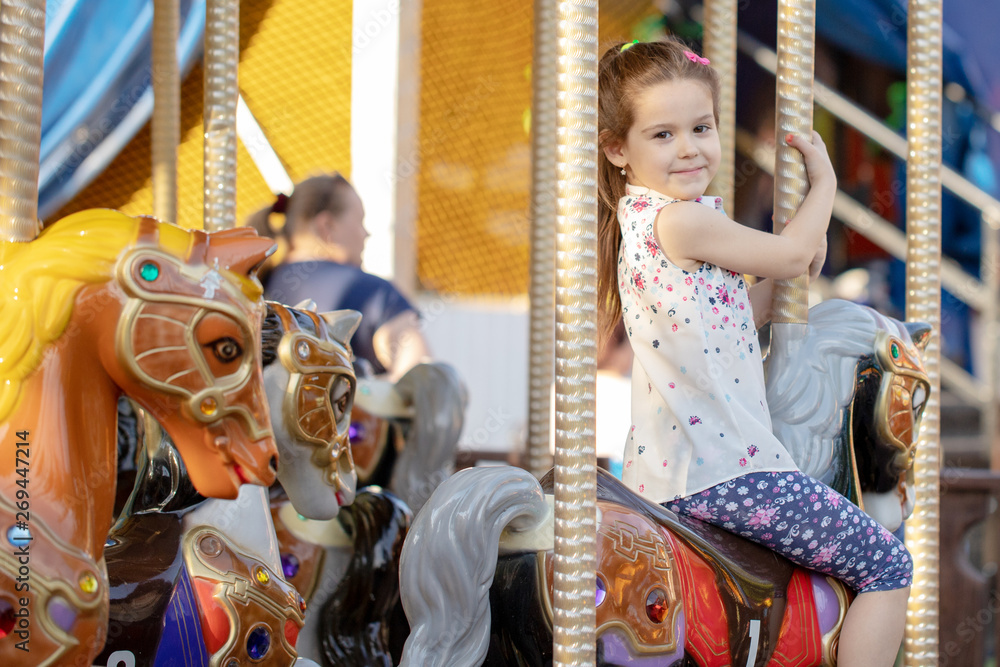 Adorable little toddler girl riding on animal on roundabout carousel in amusement park. Happy healthy baby child having fun outdoors on sunny day. Family weekend or vacations