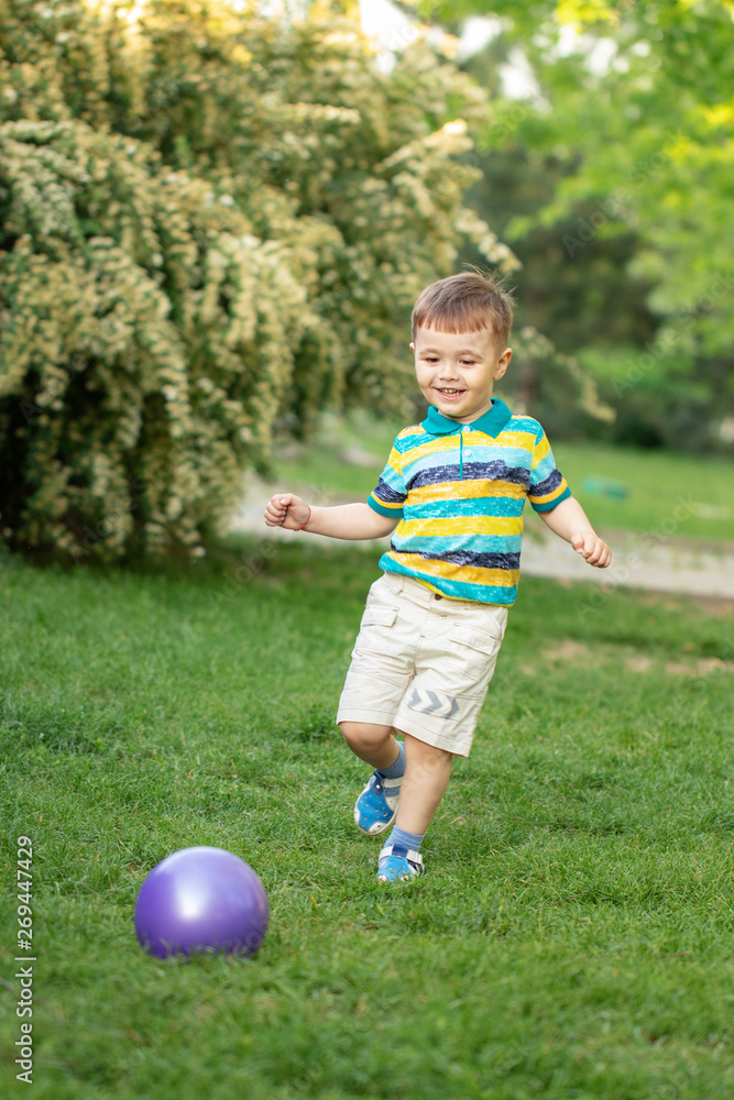 Happy little boy playing with inflatable ball on the grass in the park Happy little boy playing with inflatable ball on the grass in the park