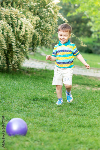 Happy little boy playing with inflatable ball on the grass in the park