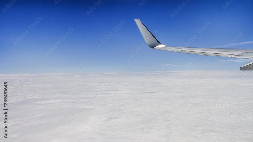 Fototapeta premium Close up of window with airplane wing. Beautiful cloudscape with clear blue sky.