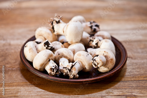 Fresh raw organic champignons on brown ceramic plate on wooden table.