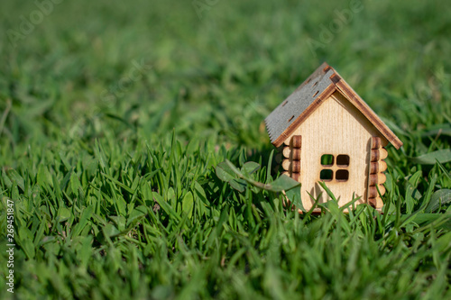 Toy wooden house on the bright grass in sunny weather. Copy space. Real estate concept, business loan financing concept, new house concept.